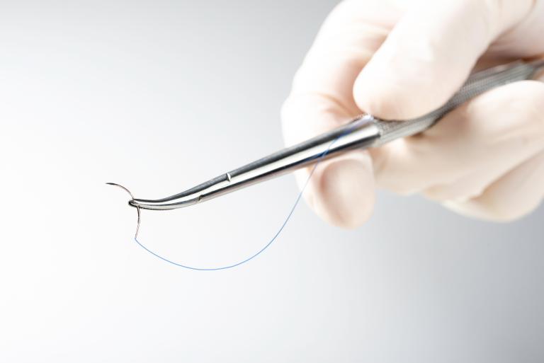 Doctor,holding,needle,holder,on,white,background.,suture,thread.,nylon